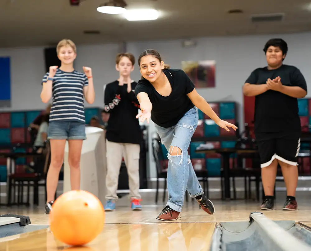 Smiling teen bowling with friends cheering behind her at Bel-Air Bowl in Belleville, IL - Youth Leagues