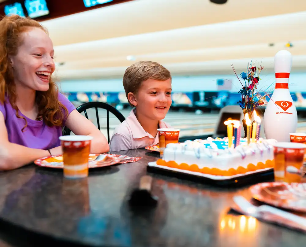Kids smiling at a birthday cake with lit candles beside a bowling pin centerpiece at Bel-Air Bowl in Belleville, IL - Birthday Parties
