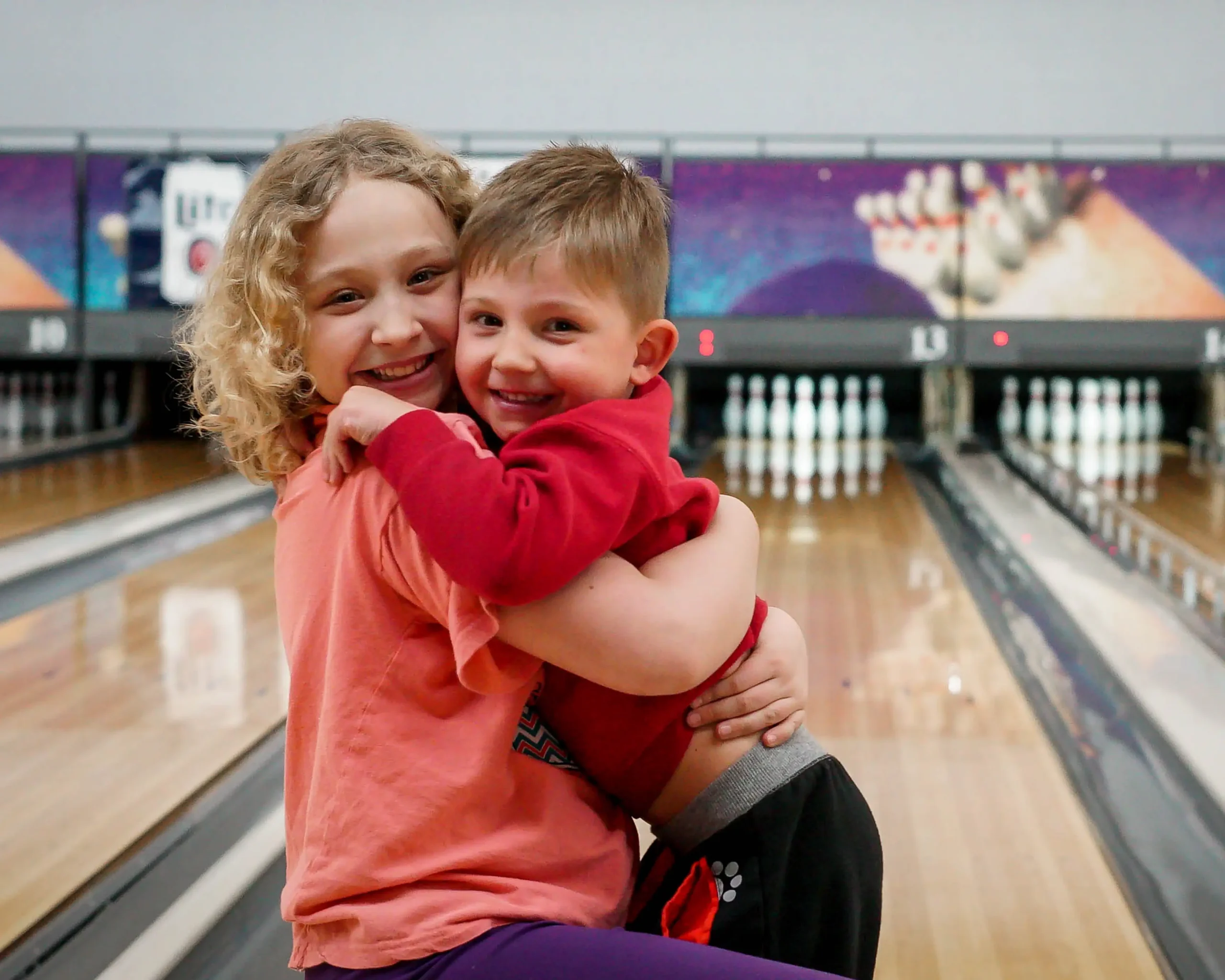 Two smiling children hugging in front of the bowling lanes at Bel-Air Bowl in Belleville, IL - Kid Bowl Free Program