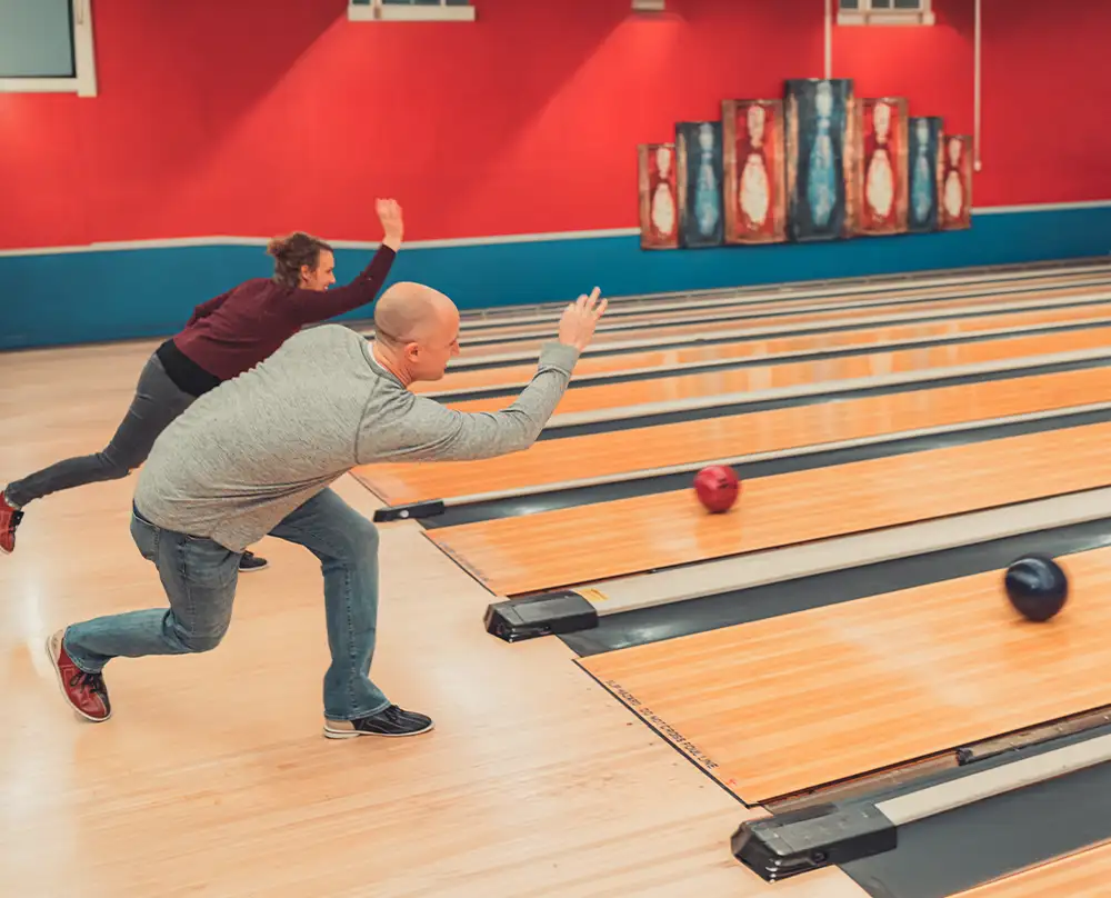 Man and woman in Adult Bowling League releasing bowling balls on side-by-side lanes at Bel-Air Bowl in Belleville, IL