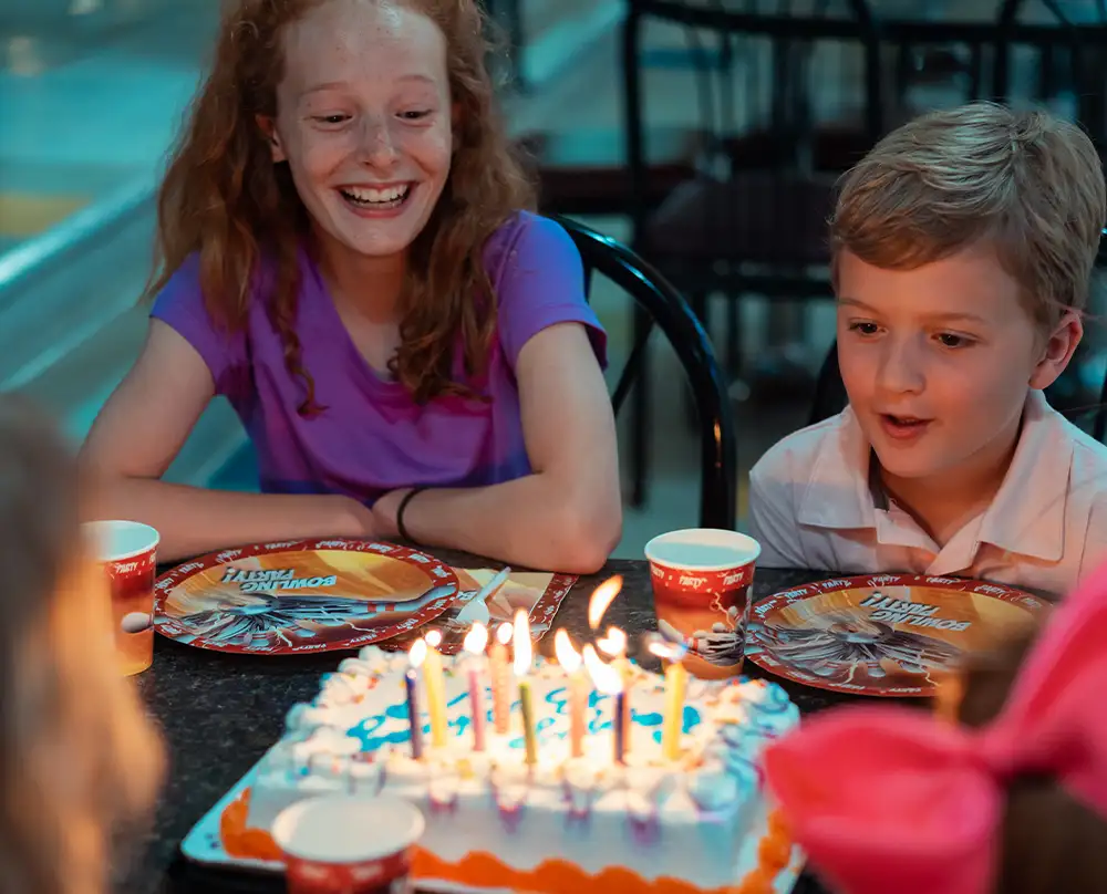 Kids gathered around a birthday cake with lit candles and bowling party plates at Bel-Air Bowl in Belleville, IL