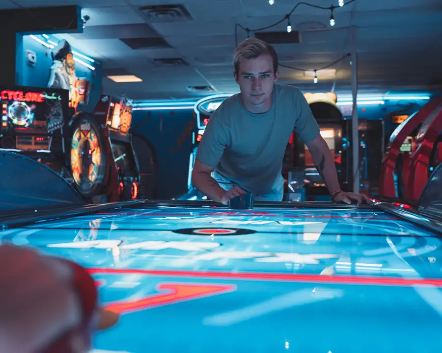 Young man leaning over a glowing blue air hockey table in the arcade at Bel-Air Bowl in Belleville, IL