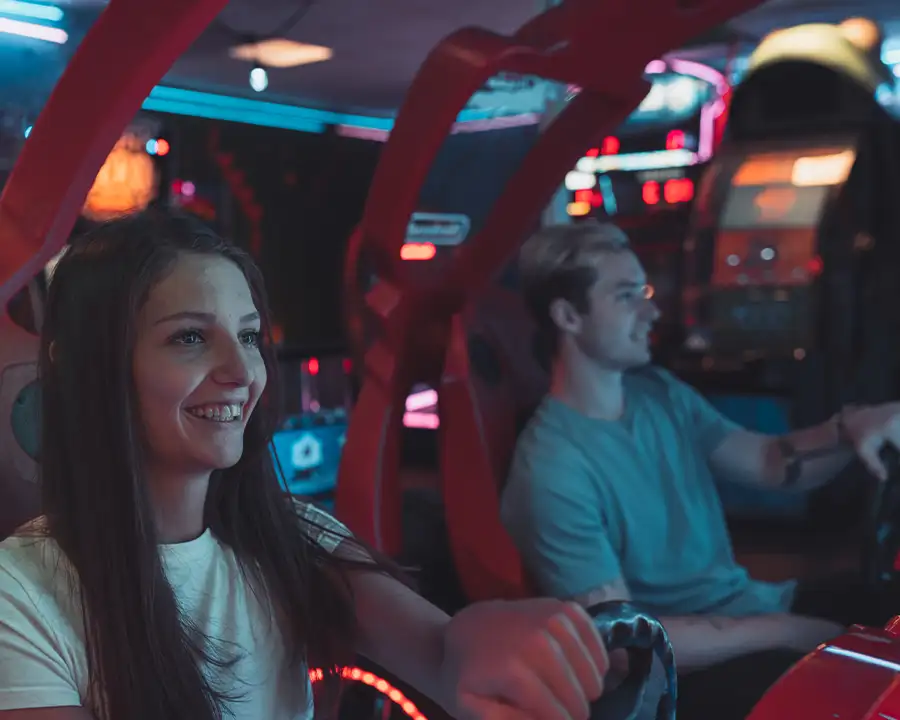 Smiling woman and man sitting in red racing arcade game seats at Bel-Air Bowl in Belleville, IL
