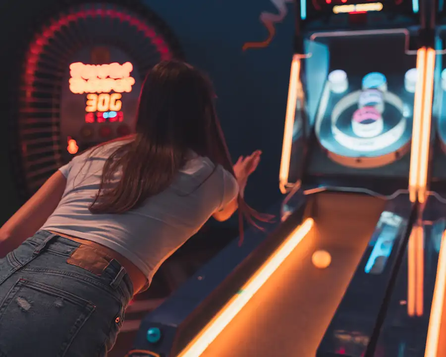Woman rolling a ball down a neon-lit skee-ball lane in the arcade at Bel-Air Bowl in Belleville, IL