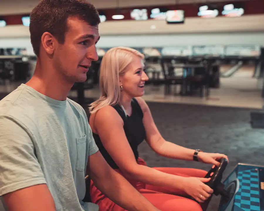 Man and woman laughing while steering a racing arcade game at Bel-Air Bowl in Belleville, IL