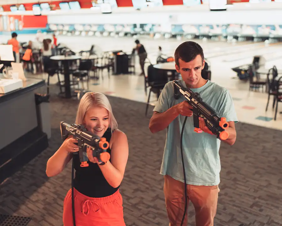 Man and woman playing a shooter arcade game with the bowling lanes behind them at Bel-Air Bowl in Belleville, IL