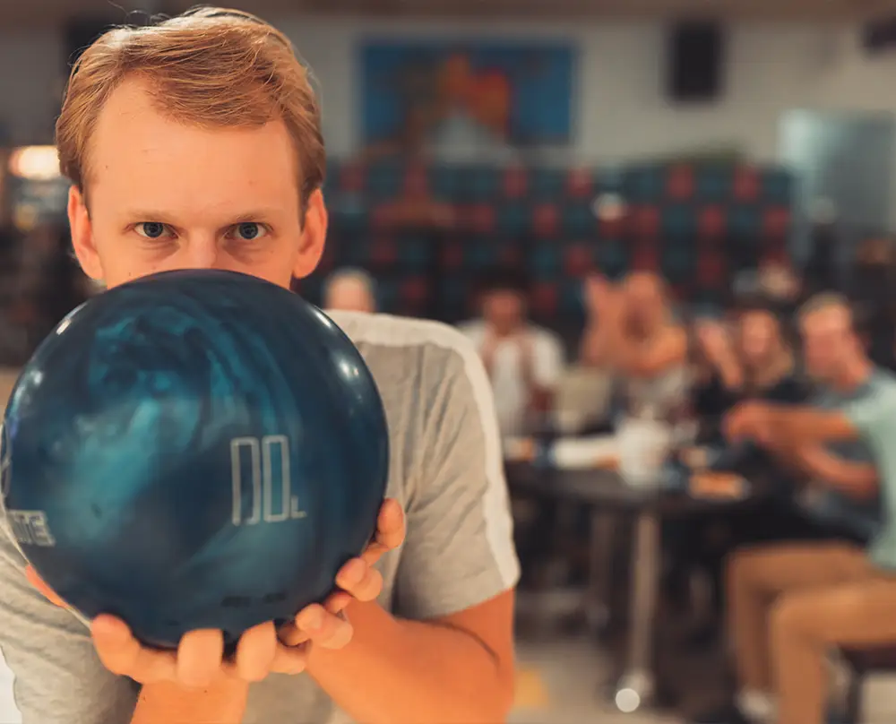 Bowler holding a bowling ball with friends in the background at Bel-Air Bowl in Belleville, IL.